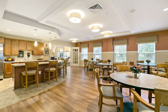 A well-lit dining and kitchen area with wooden flooring and neatly arranged tables and chairs.