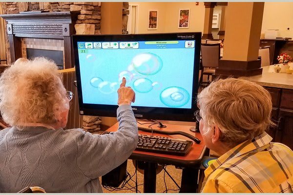 An elderly person and a child interact with an educational program on a computer.