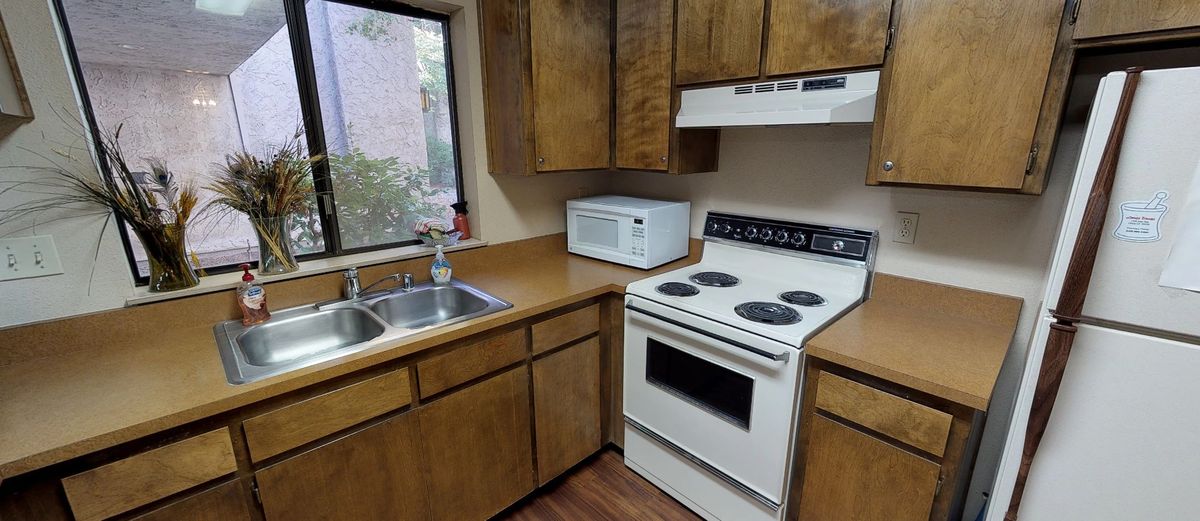 A compact kitchen with wooden cabinets, equipped with a stove, microwave, and sink.