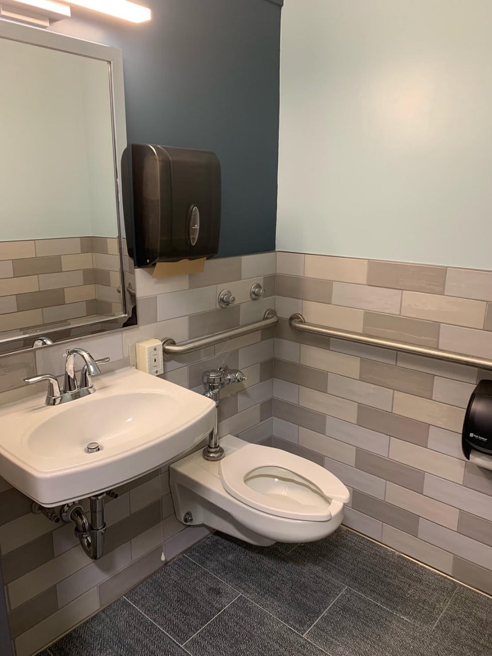 A clean and modern bathroom with a sink, toilet, and safety handrails.