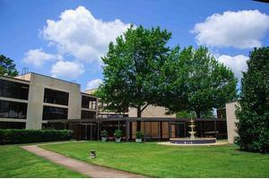 A modern building with a fountain and lush green trees under a cloudy blue sky.