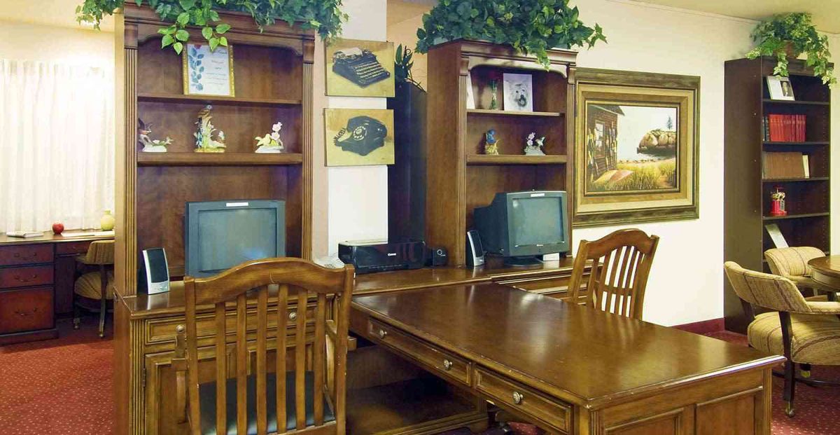 A cozy office setup featuring wooden furniture, computers, and decorative plants.