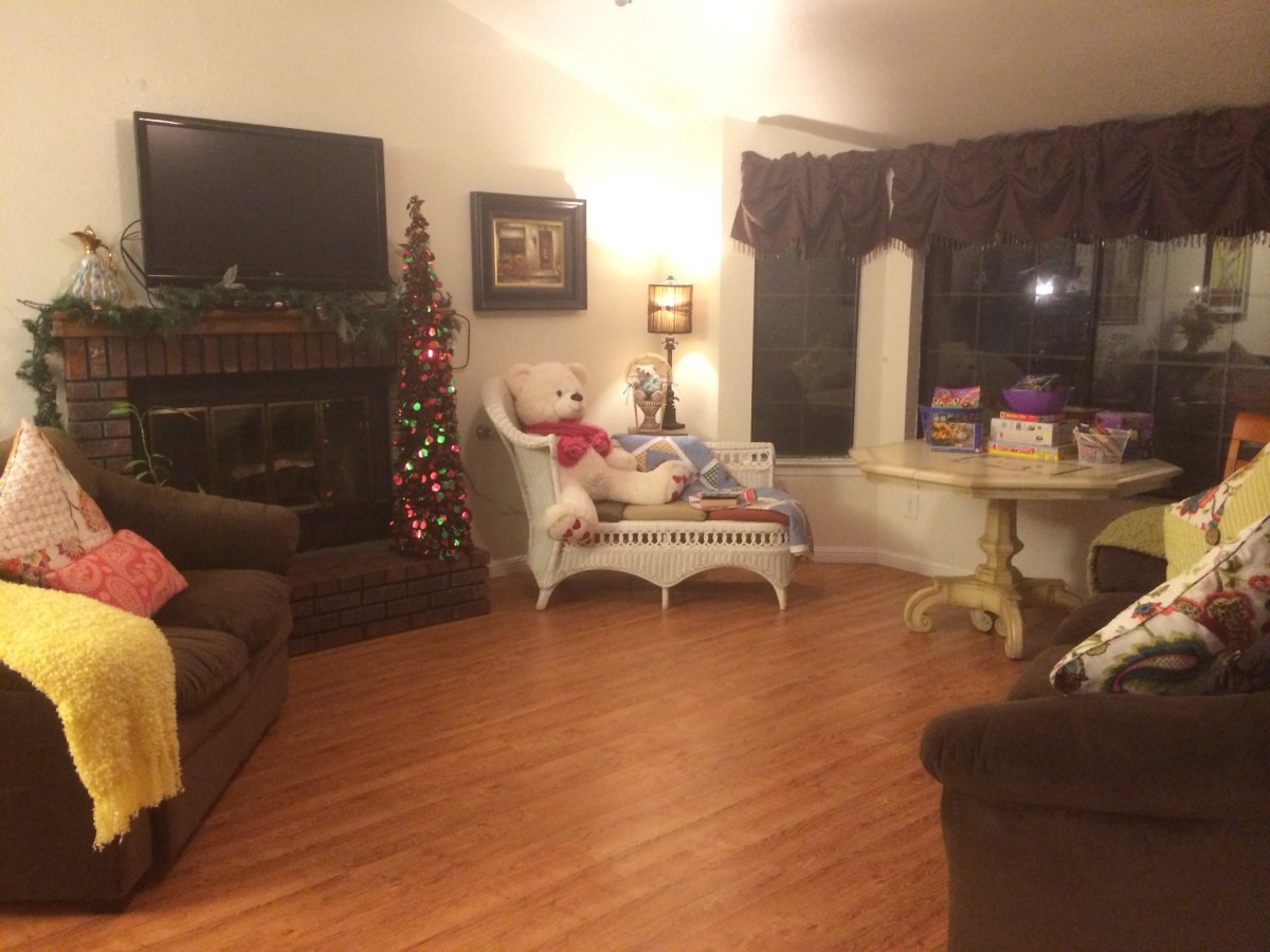 A cozy living room decorated for Christmas with a small tree, teddy bear, and gifts.
