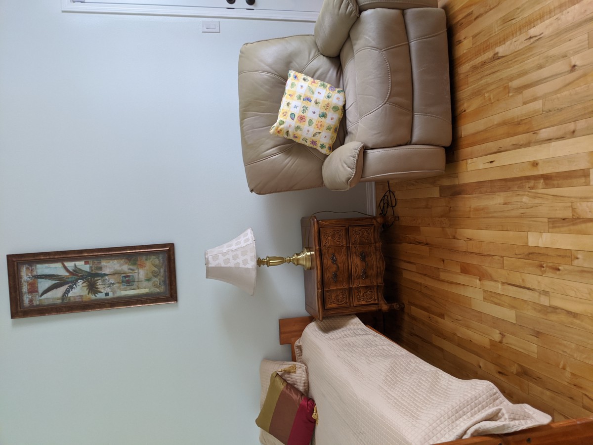 A cozy living room with a beige armchair, a side table with a lamp, and a decorative pillow on the seat.