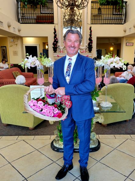 A man in a suit smiling and holding a basket of flowers indoors.