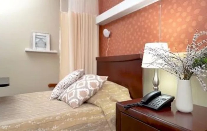 A cozy bedroom featuring a bed with patterned pillows, a lamp on a nightstand, and warm decor.