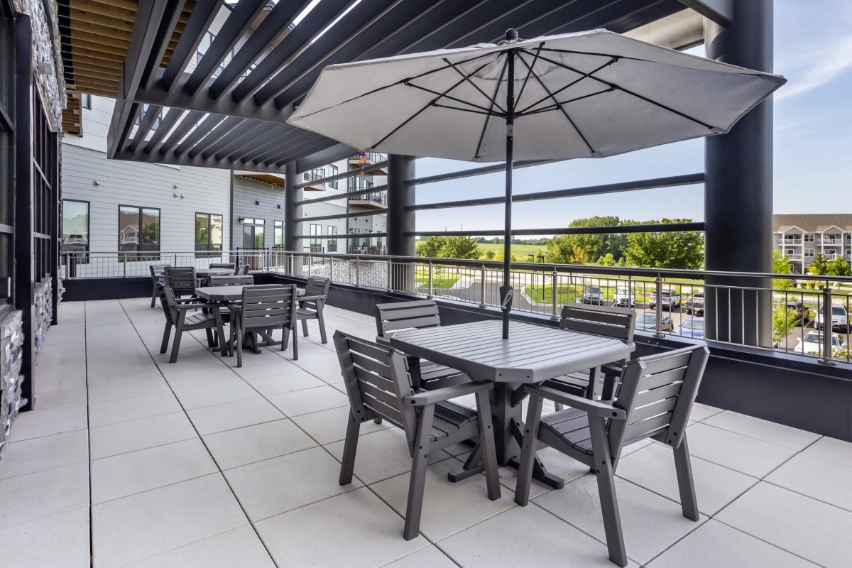 A modern outdoor patio with tables, chairs, and umbrellas, offering a scenic balcony view.