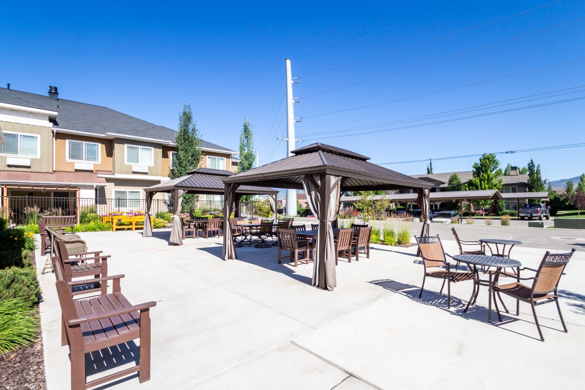 A sunny outdoor patio area with gazebos, chairs, and tables in front of a building.