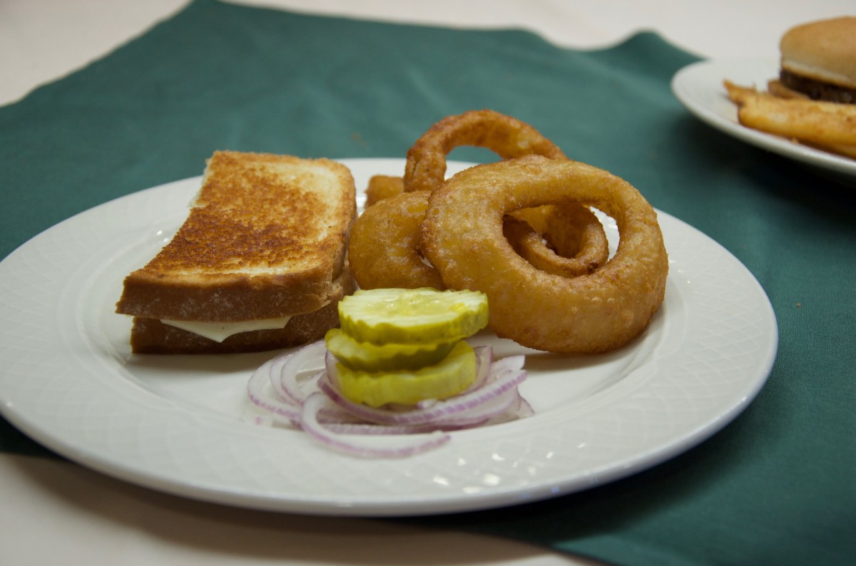 A plate with a sandwich, crispy onion rings, pickle slices, and raw red onion.