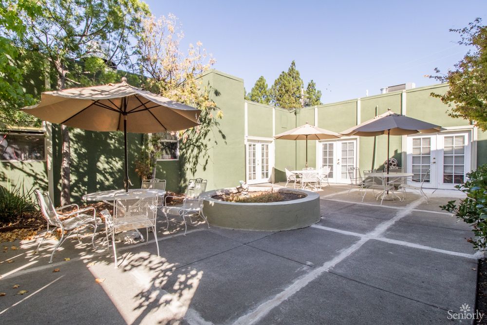 A sunny outdoor patio with tables, chairs, and umbrellas next to a green building.