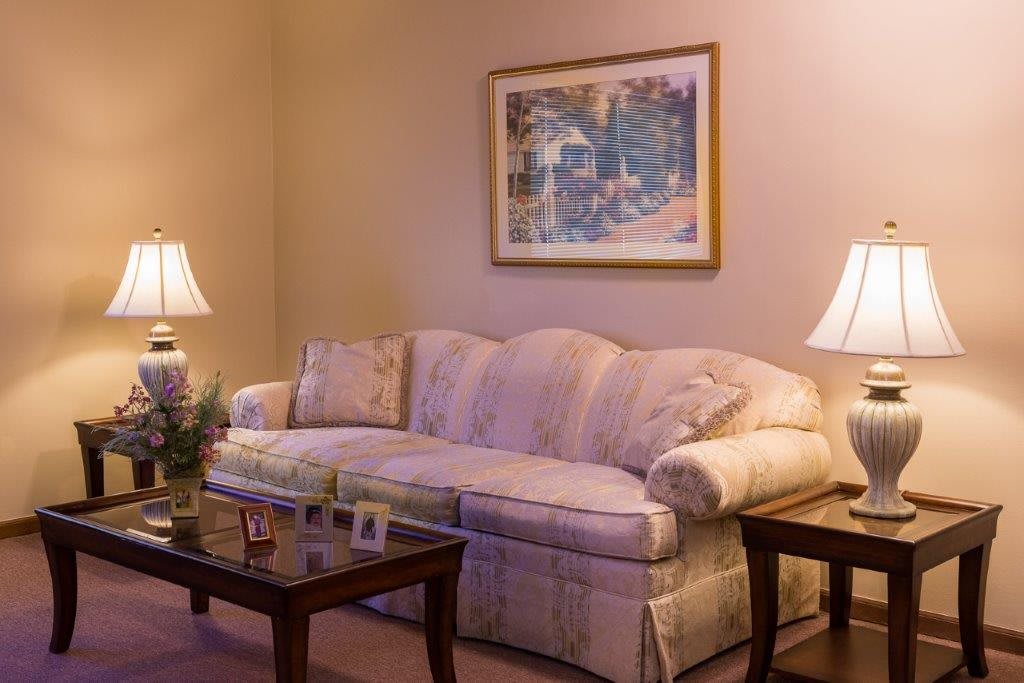 A cozy living room featuring a plush sofa, two table lamps, and a painting on the wall.