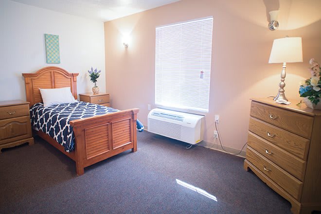 A cozy bedroom with a single bed, wooden furniture, and a window letting in natural light.