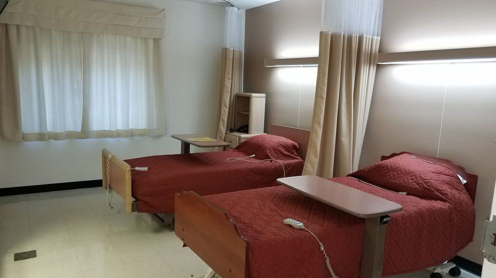A hospital room featuring two patient beds with red bedding, separated by curtains.
