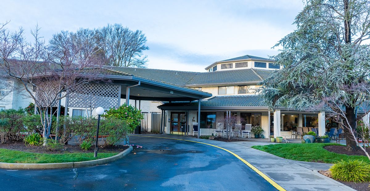 The photo shows the front entrance of a building with a covered driveway and landscaped surroundings.