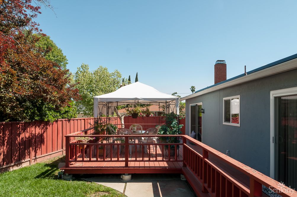 A cozy backyard deck with a canopy and outdoor seating, surrounded by a wooden fence on a sunny day.