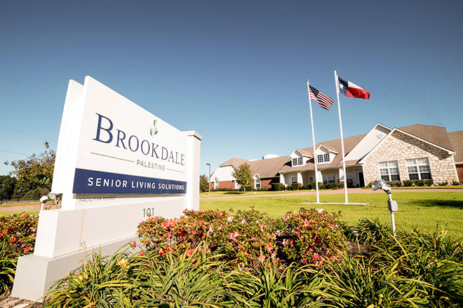 A senior living community facility with a welcoming sign and flags in the front.