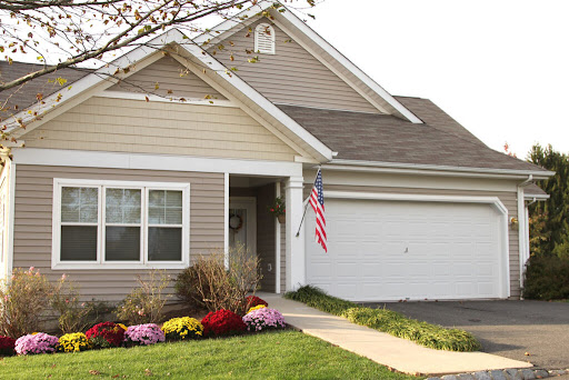 A charming suburban home with colorful flower beds and an American flag.