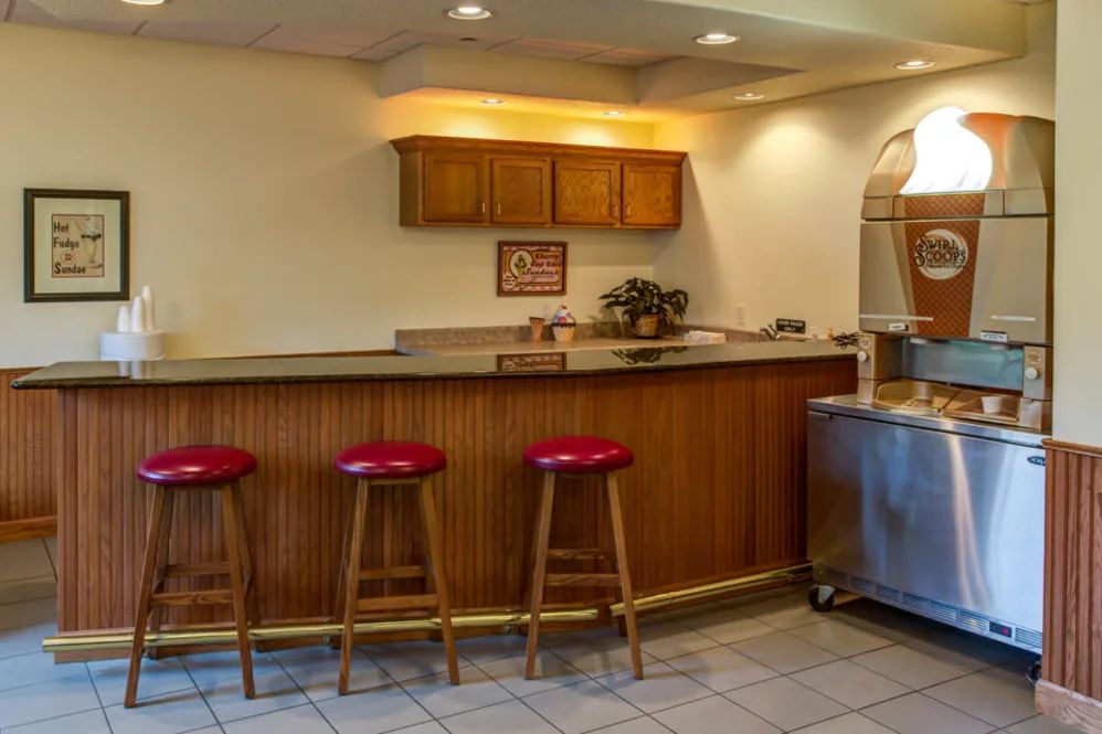 A cozy bar area with three red stools, a wooden counter, and overhead cabinets.