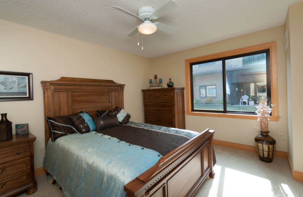 A cozy bedroom featuring a wooden bed and dresser, with natural light streaming through a large window.