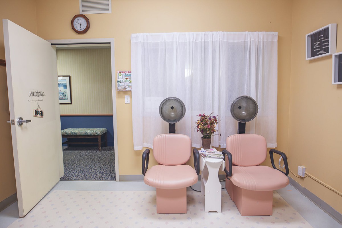 A vintage-style salon waiting area with two pink chairs and hair dryers, adorned with flowers.