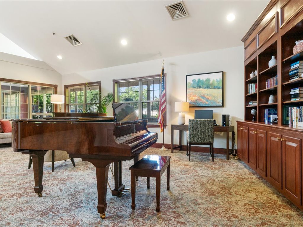 A cozy living room with a grand piano and a library corner.