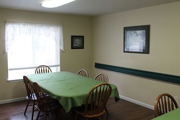 A dining room with a green tablecloth-covered table and wooden chairs, with framed pictures on the walls.