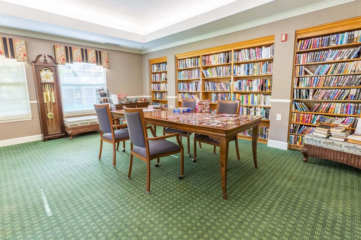 A cozy library reading room with a large table, surrounded by bookshelves and upholstered chairs.