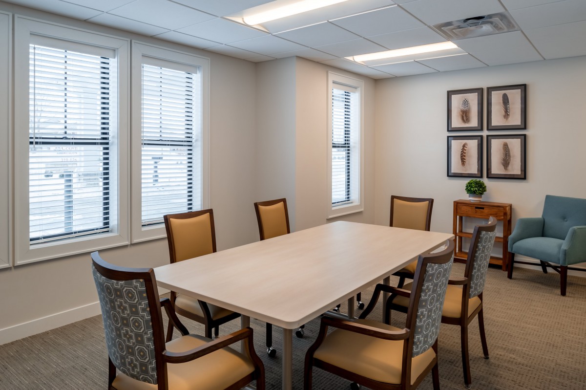 A well-lit conference room featuring a long table surrounded by chairs, with windows and artwork on the walls.