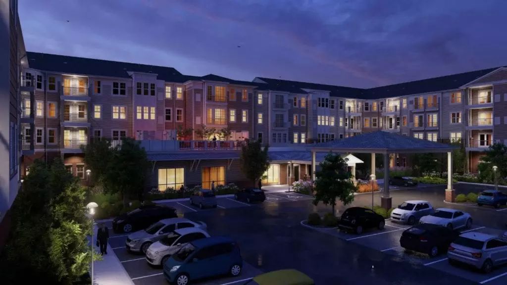 A residential building with illuminated windows and a parking lot at night.