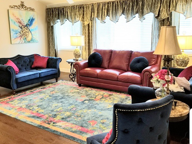 A cozy living room with a mix of red and blue sofas, decorative pillows, and a colorful carpet.