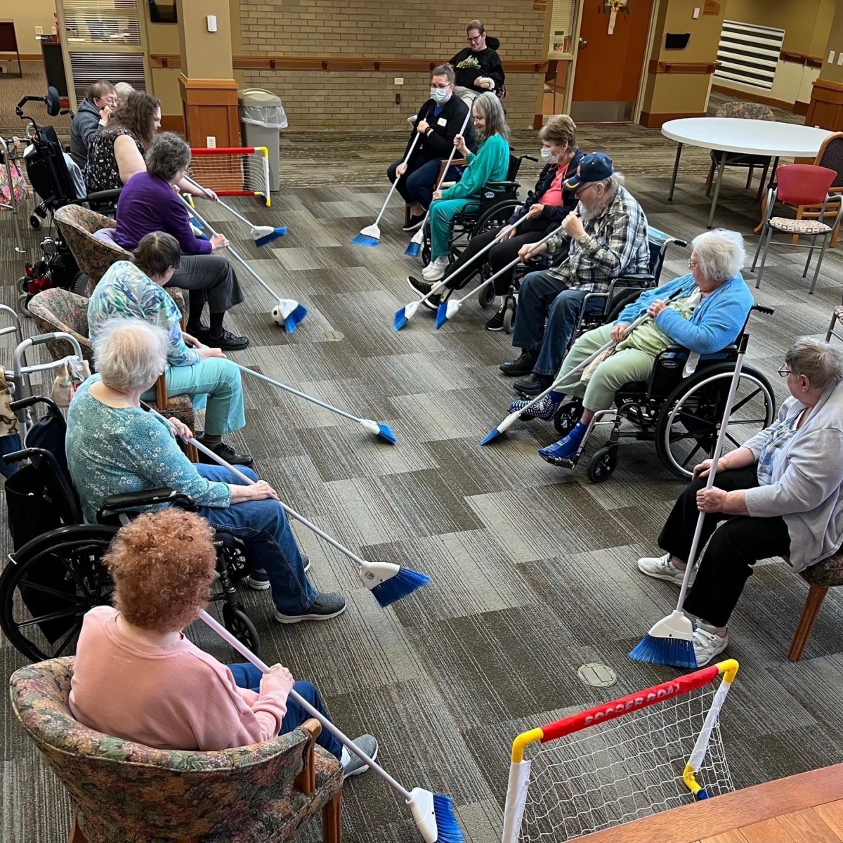 A group of seniors participating in a seated exercise session indoors, some using wheelchairs.