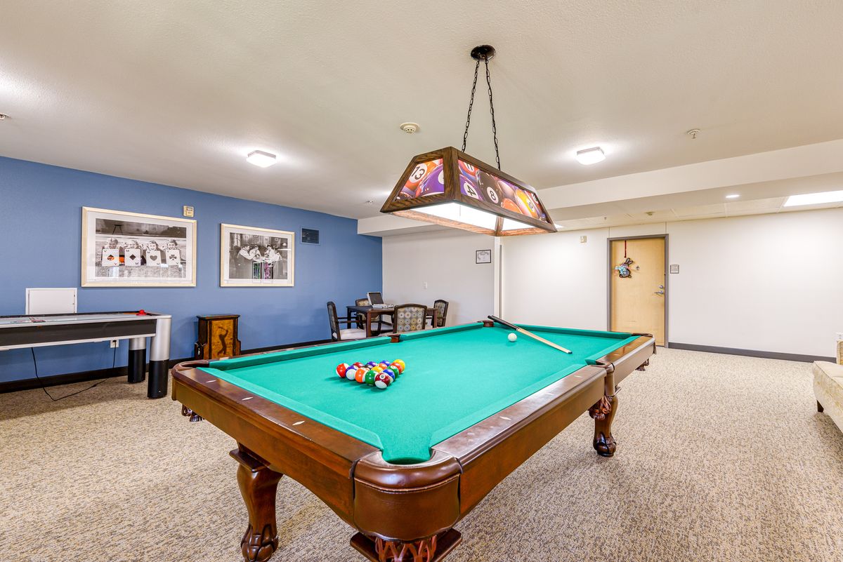 A well-lit game room featuring a pool table with cues and racked balls ready for play.