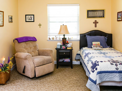 A cozy bedroom featuring a comfy armchair, a neatly made bed with a decorative quilt, and a nightstand with personal items.