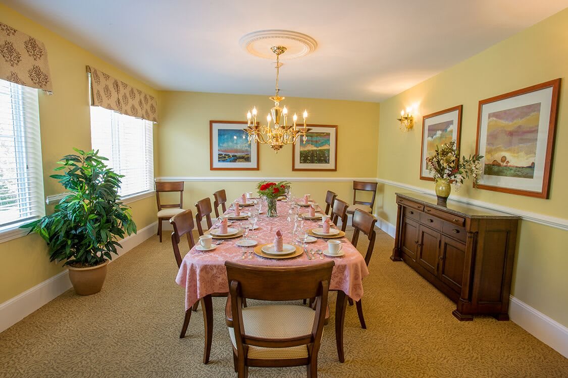 A cozy dining room with a large table set for a meal, featuring a chandelier and artwork on the walls.