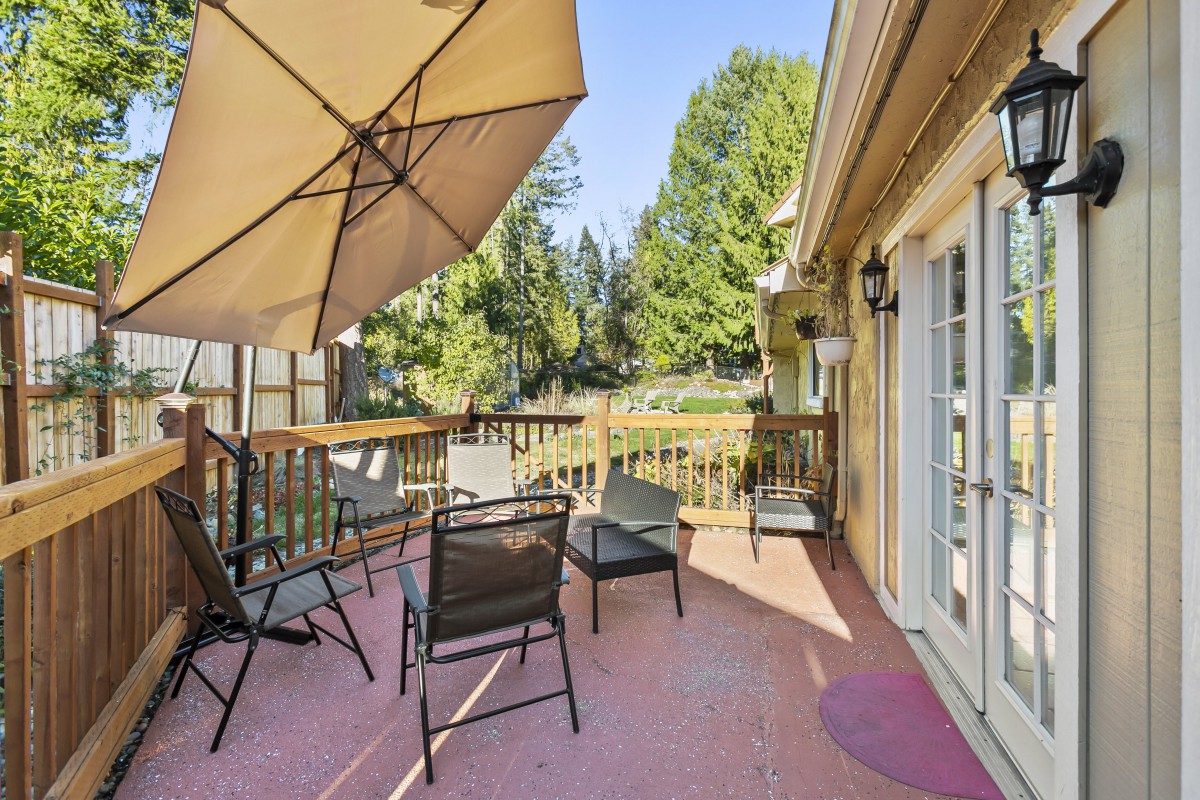 A sunny deck with outdoor furniture and an umbrella, surrounded by trees.