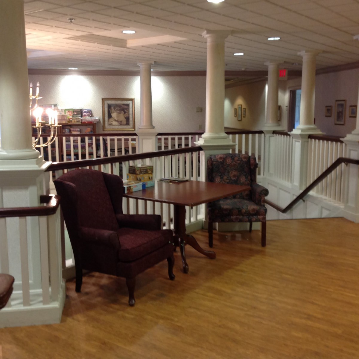 A cozy indoor seating area with chairs and a table on a wooden floor, surrounded by white railings and soft lighting.