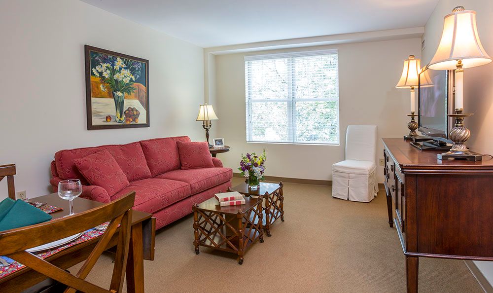 A cozy living room with a red sofa, art on the wall, and a well-lit window.