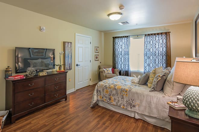 A cozy and well-decorated bedroom with a bed, wooden dresser, and patterned curtains.