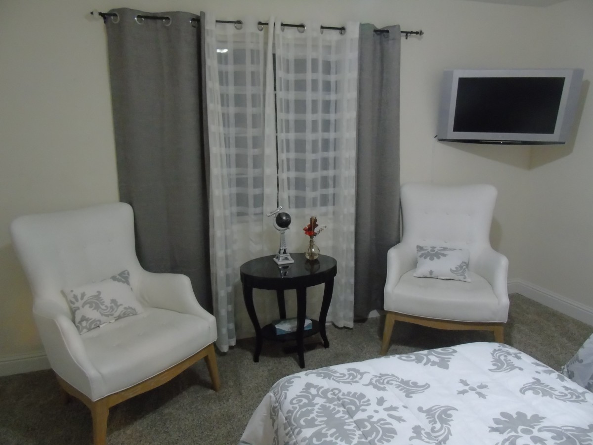 A cozy corner with two armchairs and a small table, complemented by elegant curtains and a wall-mounted television.