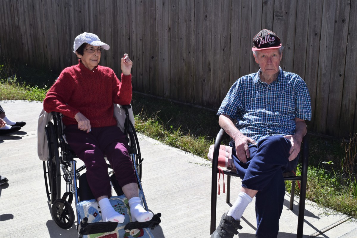 An elderly couple enjoying a sunny day outdoors, sitting together with one in a wheelchair.