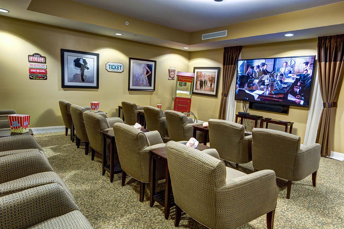 A cozy home theater room featuring rows of comfortable armchairs, a large screen TV, movie posters on the walls, and a classic popcorn machine.