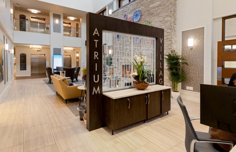 A modern lobby area with elegant furniture and plants, featuring a reception desk labeled 'Atrium Village'.