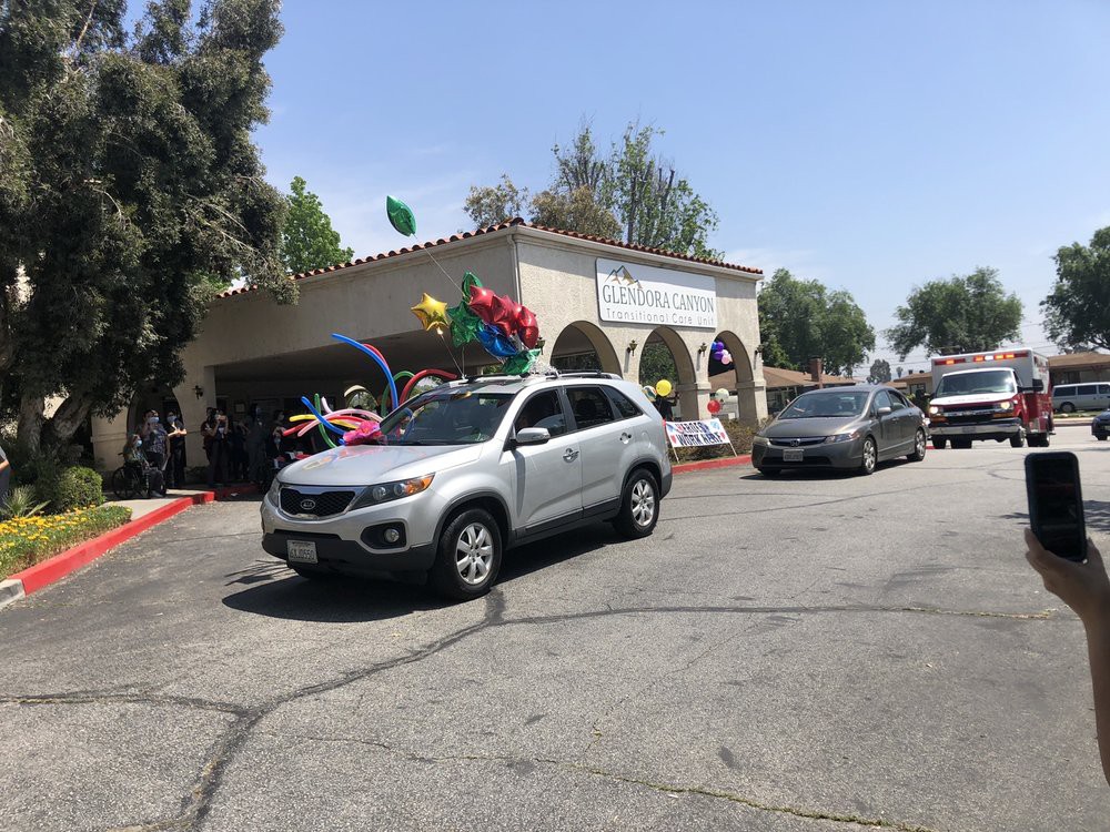 A parade of cars decorated with balloons passes by a building on a sunny day.