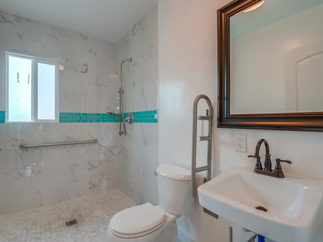 A modern bathroom featuring a walk-in shower with teal accent tiles, a toilet, a sink with a black faucet, and a large framed mirror.