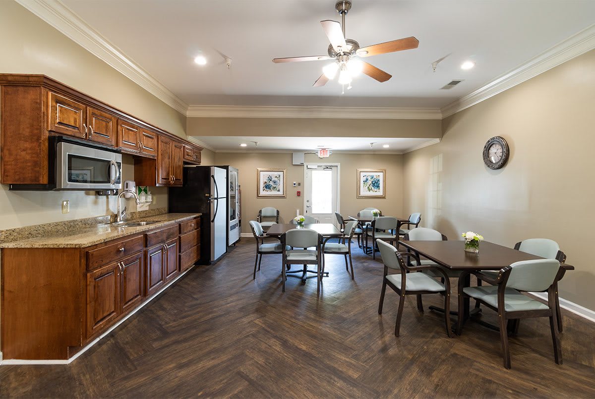 A cozy kitchen and dining area with wooden cabinets, a refrigerator, tables, chairs, and a ceiling fan.