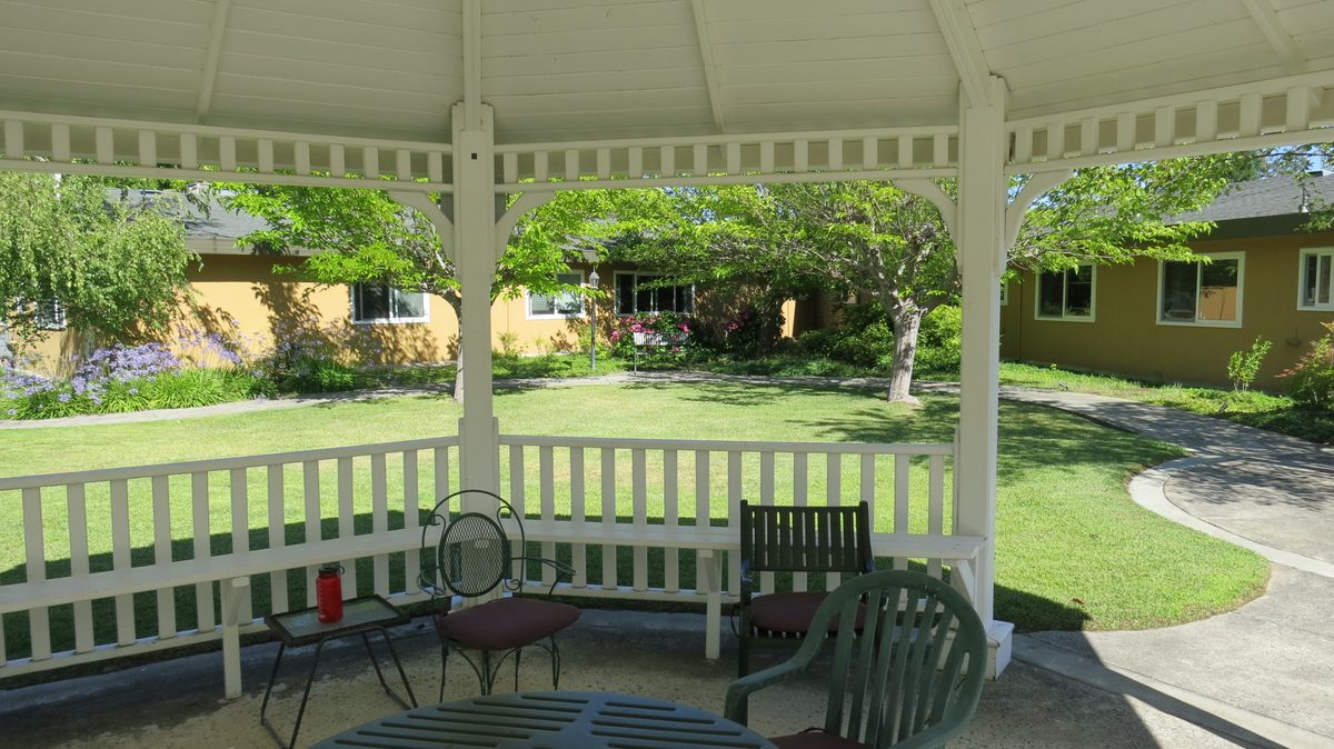 A view from inside a gazebo overlooking a garden with chairs and lush greenery.