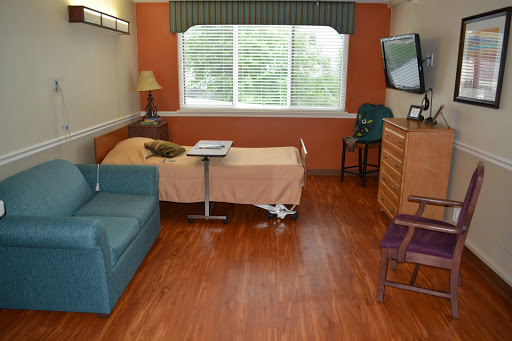A spacious hospital room featuring a bed, a sofa, and a window with natural light.
