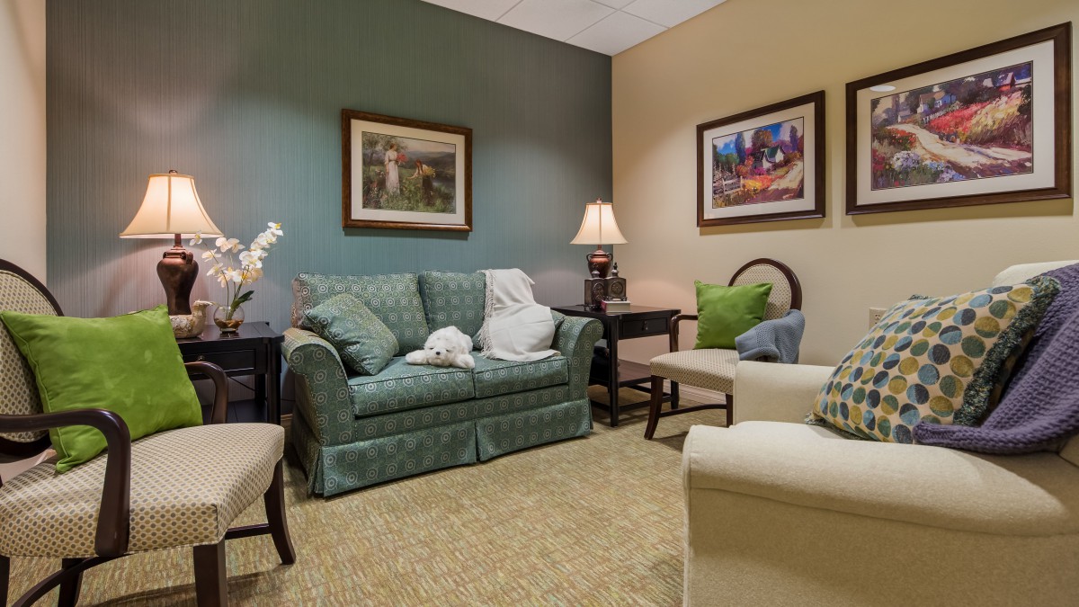A cozy living room with a green sofa, armchair, and decorative wall art.