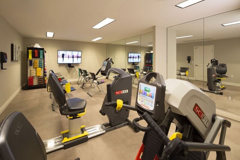 A modern gym with various fitness equipment, including exercise bicycles, and a TV on the wall.
