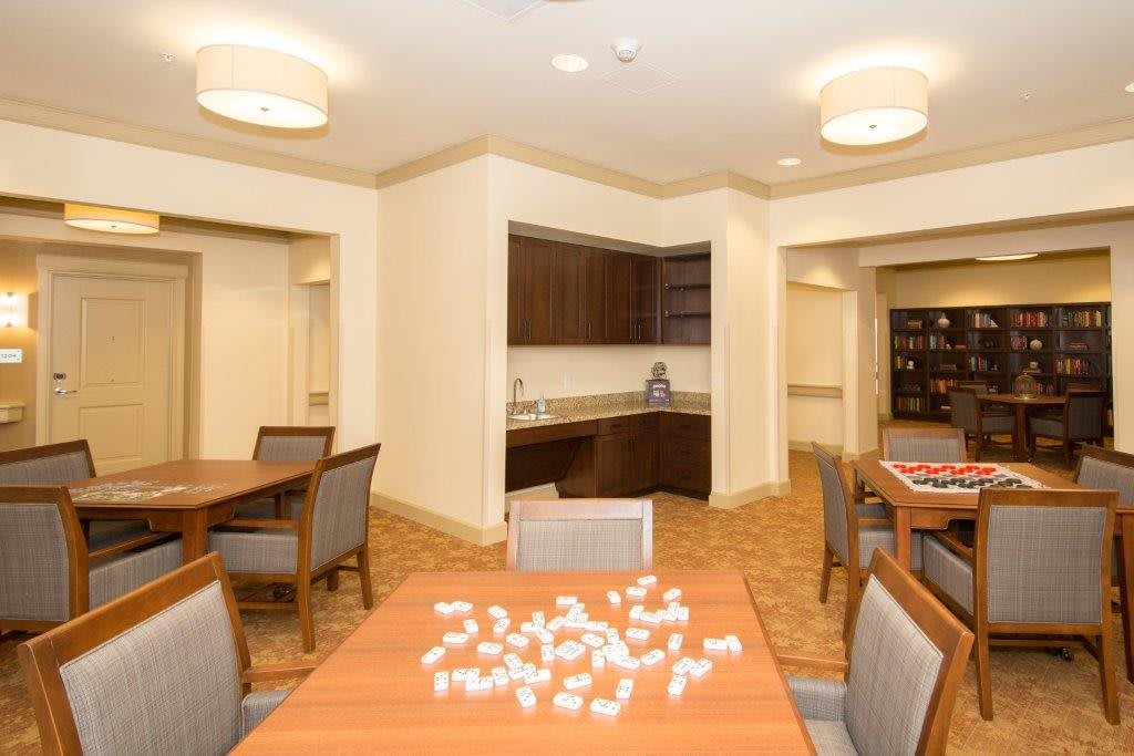 A well-lit dining area with tables and chairs, featuring a small kitchen section in the background.